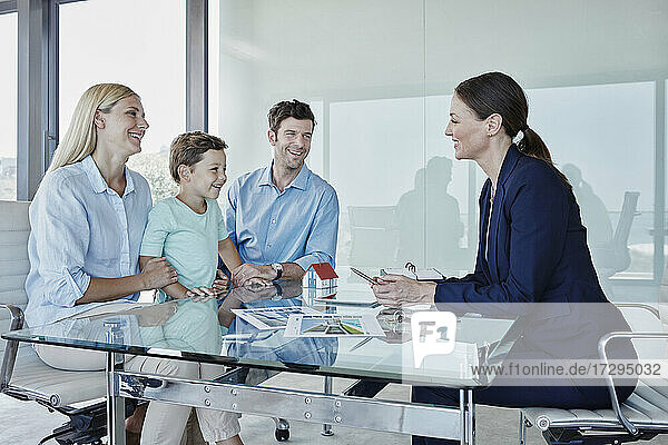 Glückliche Familie im Gespräch mit einer Immobilienmaklerin am Tisch sitzend