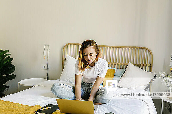 Junge Frau benutzt einen Laptop  während sie zu Hause auf dem Bett sitzt