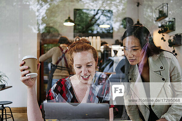 Frau mit Einweg-Kaffeebecher benutzt Laptop von Freundin in Café