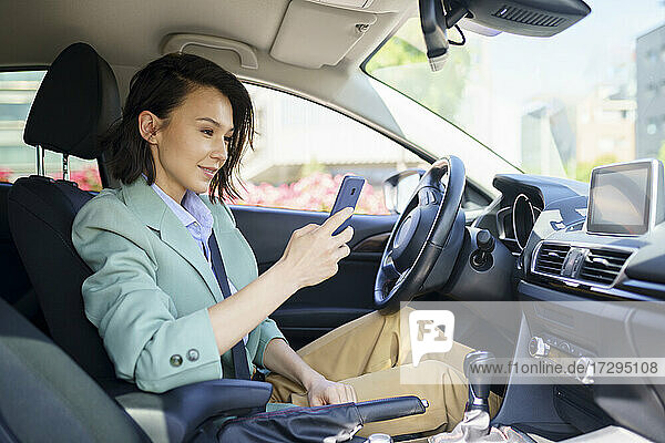 Weibliche Berufstätige  die im Auto sitzend ein Smartphone benutzen