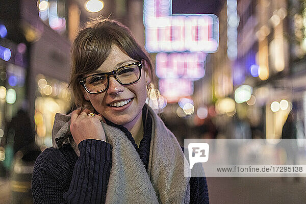 Cheerful young woman with brown hair wearing eyeglasses while standing in city