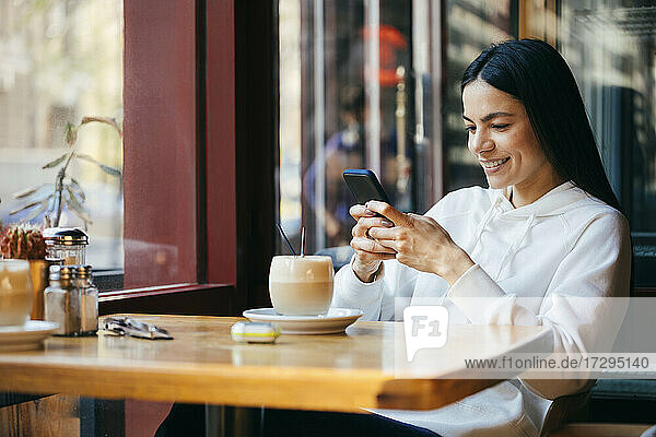 Smiling woman using mobile phone at cafe