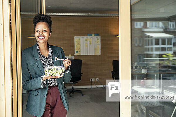 Lächelnde weibliche Fachkraft  die einen Salat isst und dabei auf den Türrahmen schaut