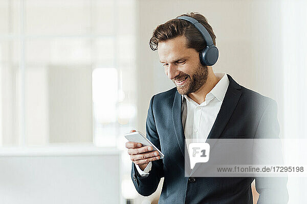 Männlicher Unternehmer mit Kopfhörern und Smartphone im Büro