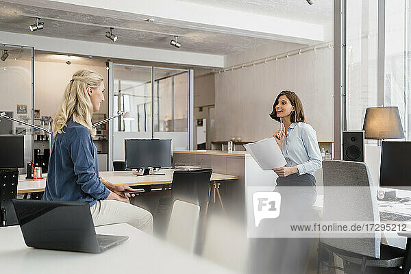 Young female entrepreneur holding documents while discussing with coworker in office