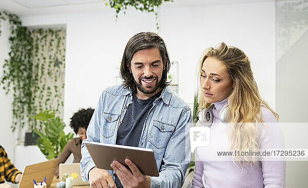 Lächelnder Geschäftsmann  der mit einer blonden Geschäftsfrau über ein Tablet im Büro diskutiert