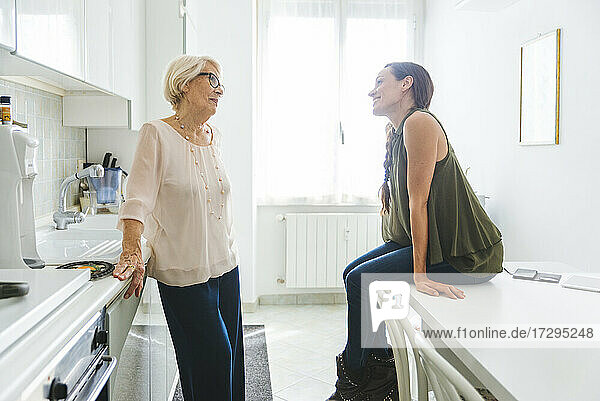 Mittlere erwachsene Frau sitzt am Tisch und spricht mit ihrer Großmutter in der Küche