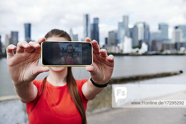 Female athlete photographing on smart phone in city