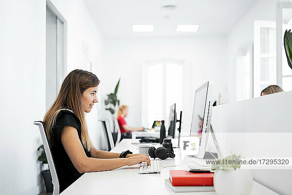 Geschäftsfrau arbeitet an einem Desktop-Computer  während sie in einem Coworking-Büro sitzt