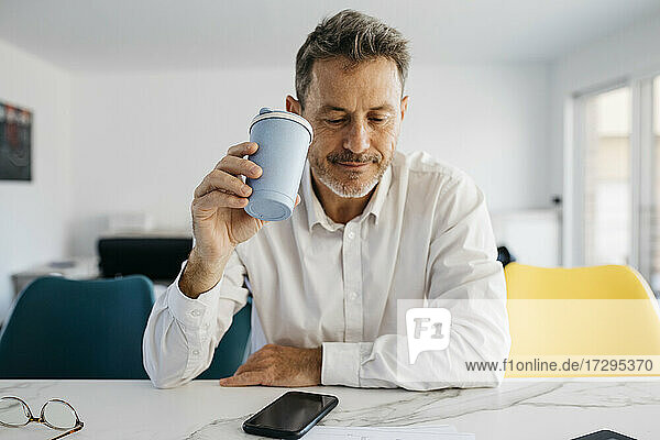 Male freelance worker holding reusable coffee cup at kitchen island