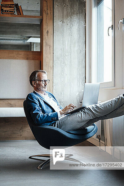 Männlicher Unternehmer mit Laptop auf dem Schoß  während er im Büro sitzt
