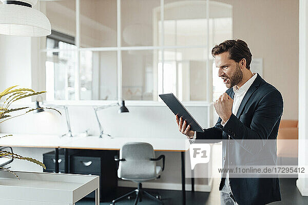 Geschäftsmann jubelt  während er ein digitales Tablet im Büro benutzt