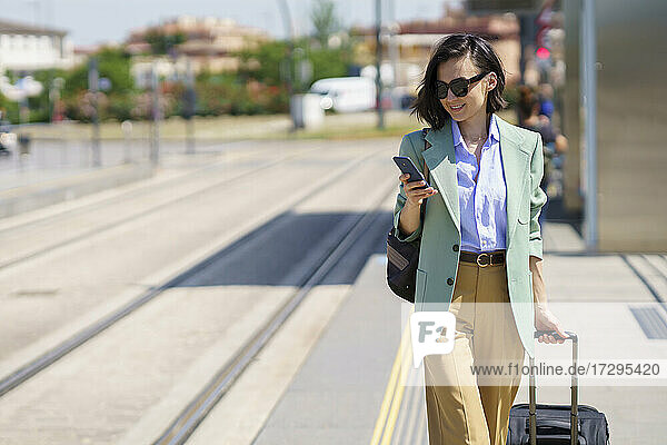 Female professional using smart phone while walking with suitcase at railroad station