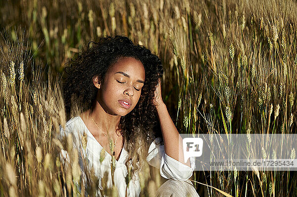 Beautiful young woman with eyes closed sitting in wheat field during sunny day