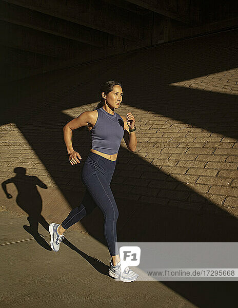 Frau joggt in der Nähe von Backsteinmauer im Sonnenlicht