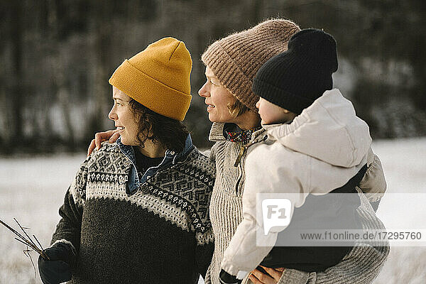 Lesbian mothers and daughter wearing knit hats while looking away