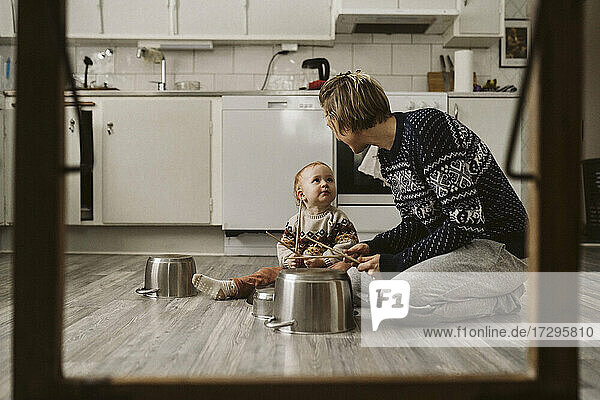 Mädchen schaut Mutter an  während sie mit Essstäbchen in der Küche zu Hause spielt