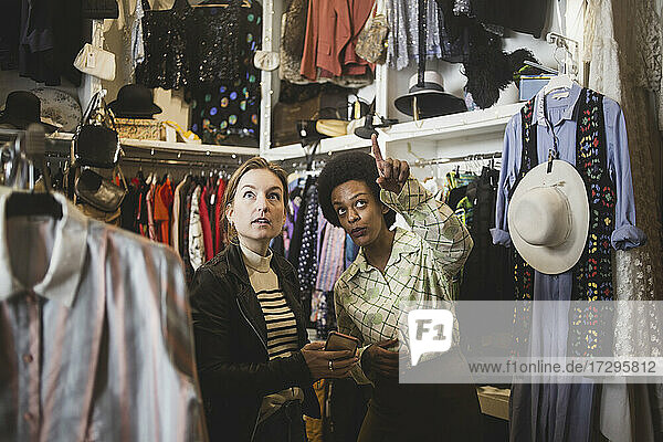 African female owner pointing while standing by customer in clothing store