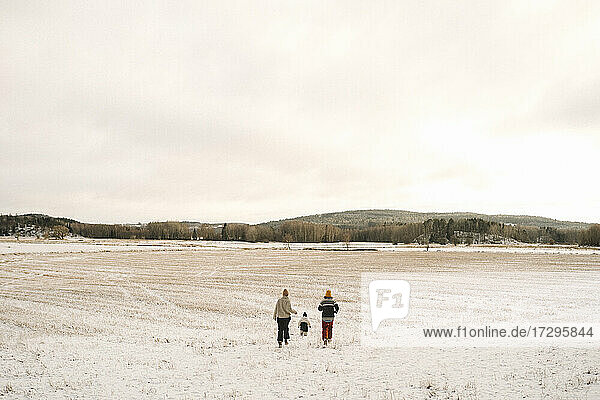Lesbian mothers and daughter running on snow covered land