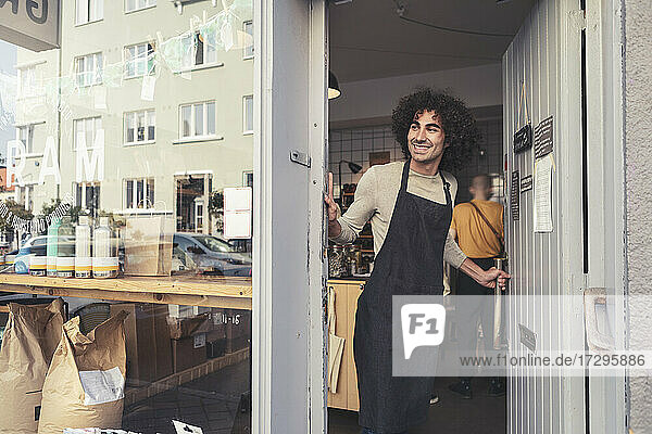 Smiling male owner opening door of organic store while looking away
