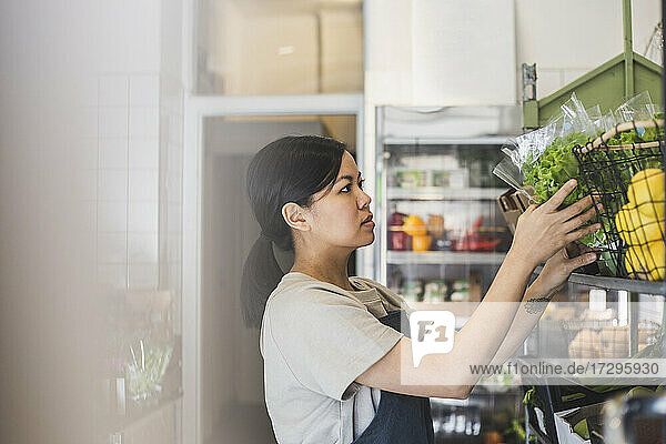Weibliche Mitarbeiterin ordnet Gemüse auf einem Regal im Laden an