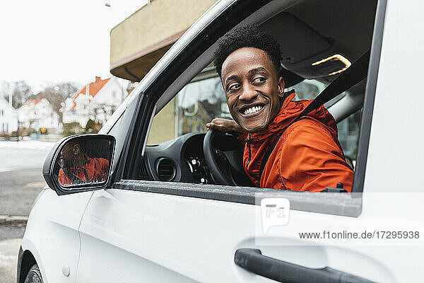 Smiling young driver looking back through window while driving delivery van