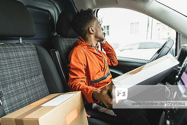 Delivery man holding package talking on mobile phone while looking away through van window