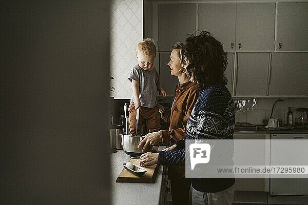 Homosexuelles Paar bereitet Essen mit Tochter stehend auf Küchentheke zu Hause