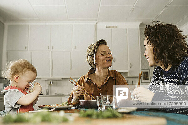 Smiling lesbian couple with daughter having lunch at home