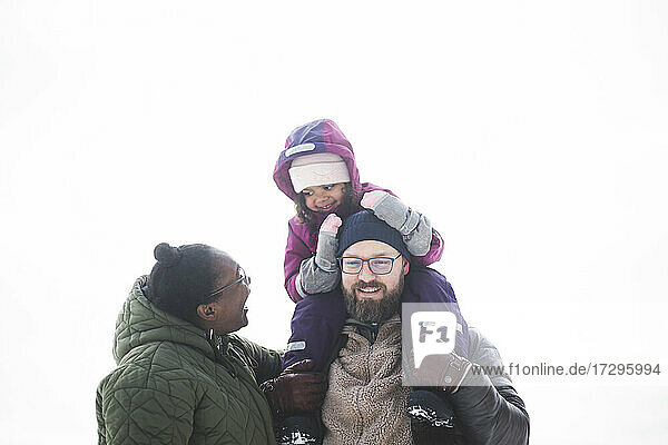 Happy woman looking at daughter sitting on man's shoulder during winter