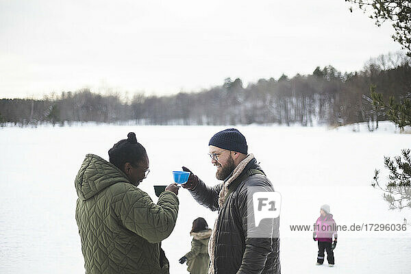 Couple with drinks while standing together outdoors during winter