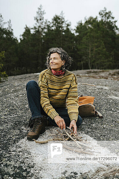 Smiling female explorer preparing campfire while sitting in forest