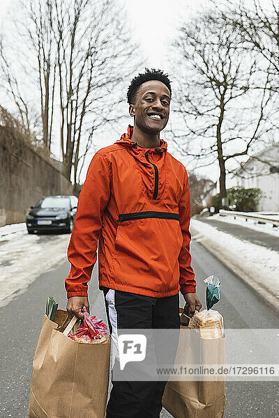 Portrait of smiling essential service male carrying paper bags while walking on road