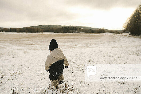 Volle Länge Rückansicht von Mädchen zu Fuß auf schneebedeckten Land während des Sonnenuntergangs