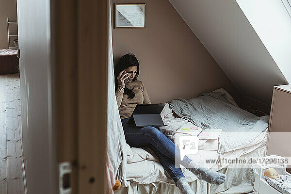 Geschäftsfrau spricht auf Smartphone  während mit digitalen Tablet im Schlafzimmer