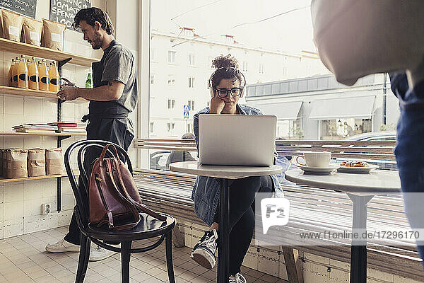 Weiblicher Kunde benutzt Laptop von männlichem Besitzer  der im Café arbeitet