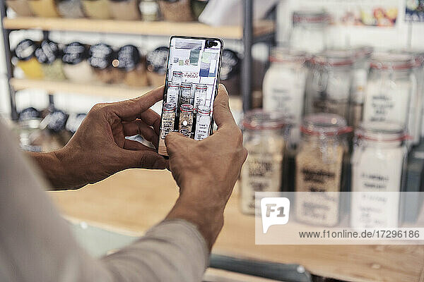 Male owner photographing jars through smart phone at organic store