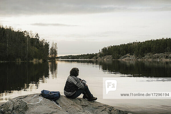 Female hiker admiring lake while sitting on rock against sky