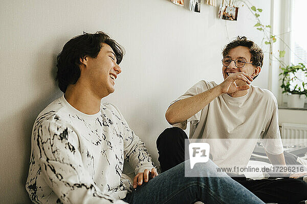 Cheerful male friends laughing while sitting in bedroom