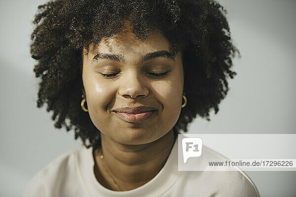 Lächelnde junge Frau mit geschlossenen Augen gegen weiße Wand