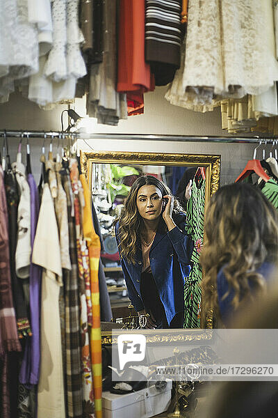 Weibliche Besitzerin schaut in den Spiegel  während sie in einem Bekleidungsgeschäft steht