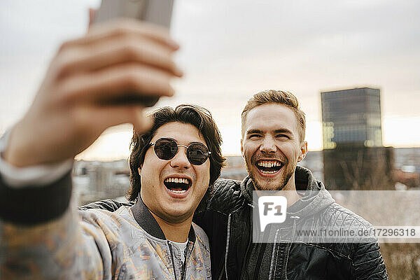 Cheerful male friends taking selfie on smart phone