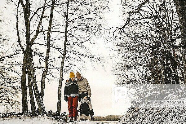 Lächelnde lesbische Mütter mit Tochter zu Fuß inmitten von kahlen Bäumen im Winter