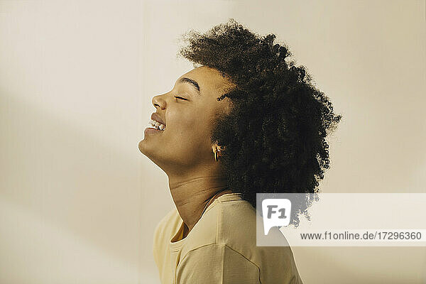 Side view of curly haired woman with eyes closed against beige wall