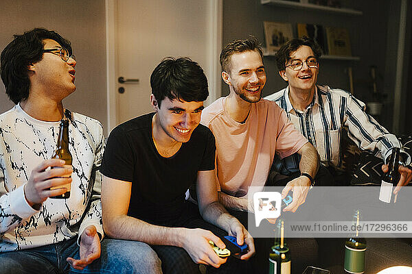 Smiling male friends with beer bottle playing video game at home