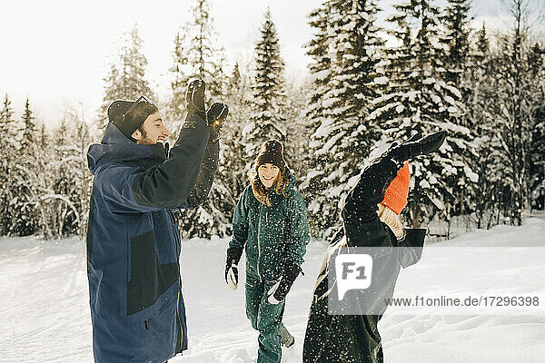 Fröhlich Mann und Frau geben High-Five von weiblichen Freund beim Spielen im Schnee im Skigebiet