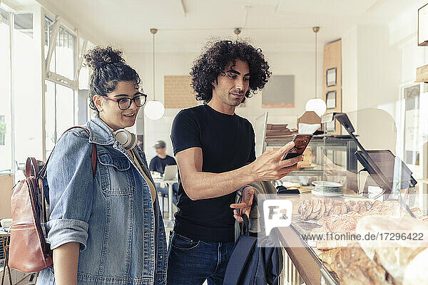 Junge Frau schaut auf männlichen Freund mit Smartphone im Café