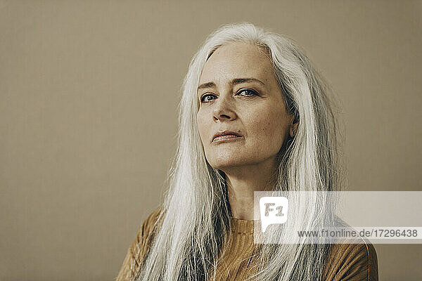 Selbstbewusste reife Frau mit weißen Haaren vor beigem Hintergrund