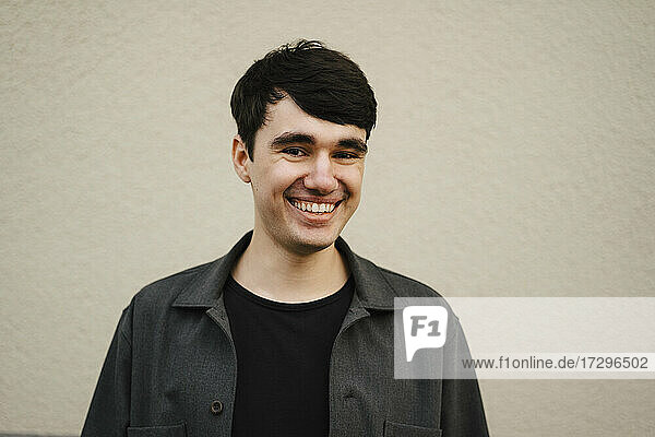 Happy young man with black hair against beige wall
