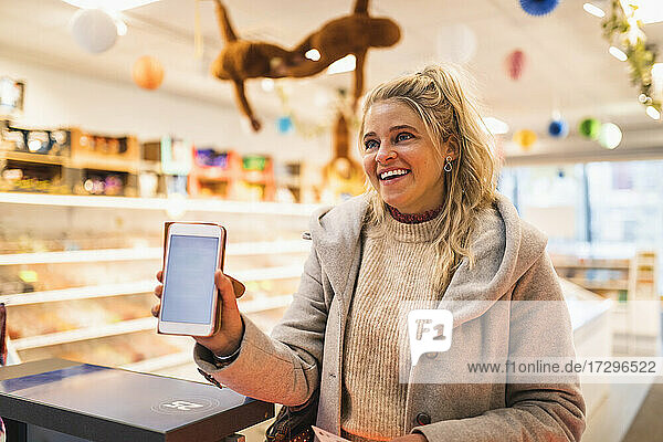 Glückliche blonde Haare Frau zeigt Smartphone im Laden